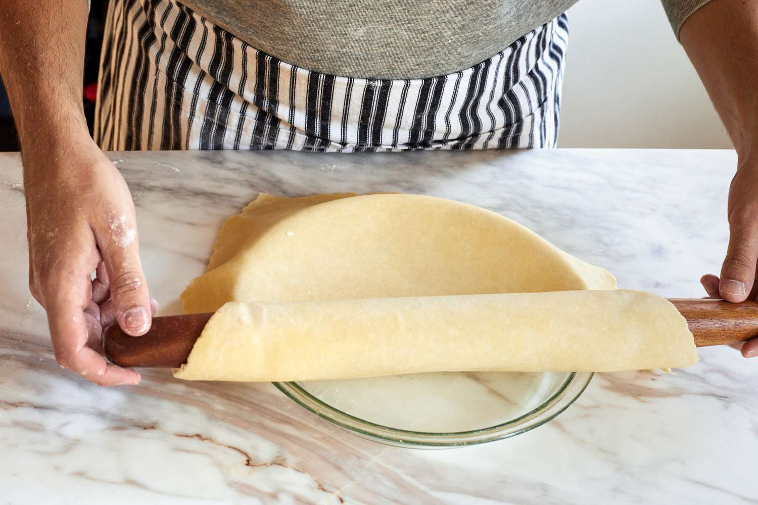 a person using a rolling pin to transfer a rolled out pie crust to a glass pie plate