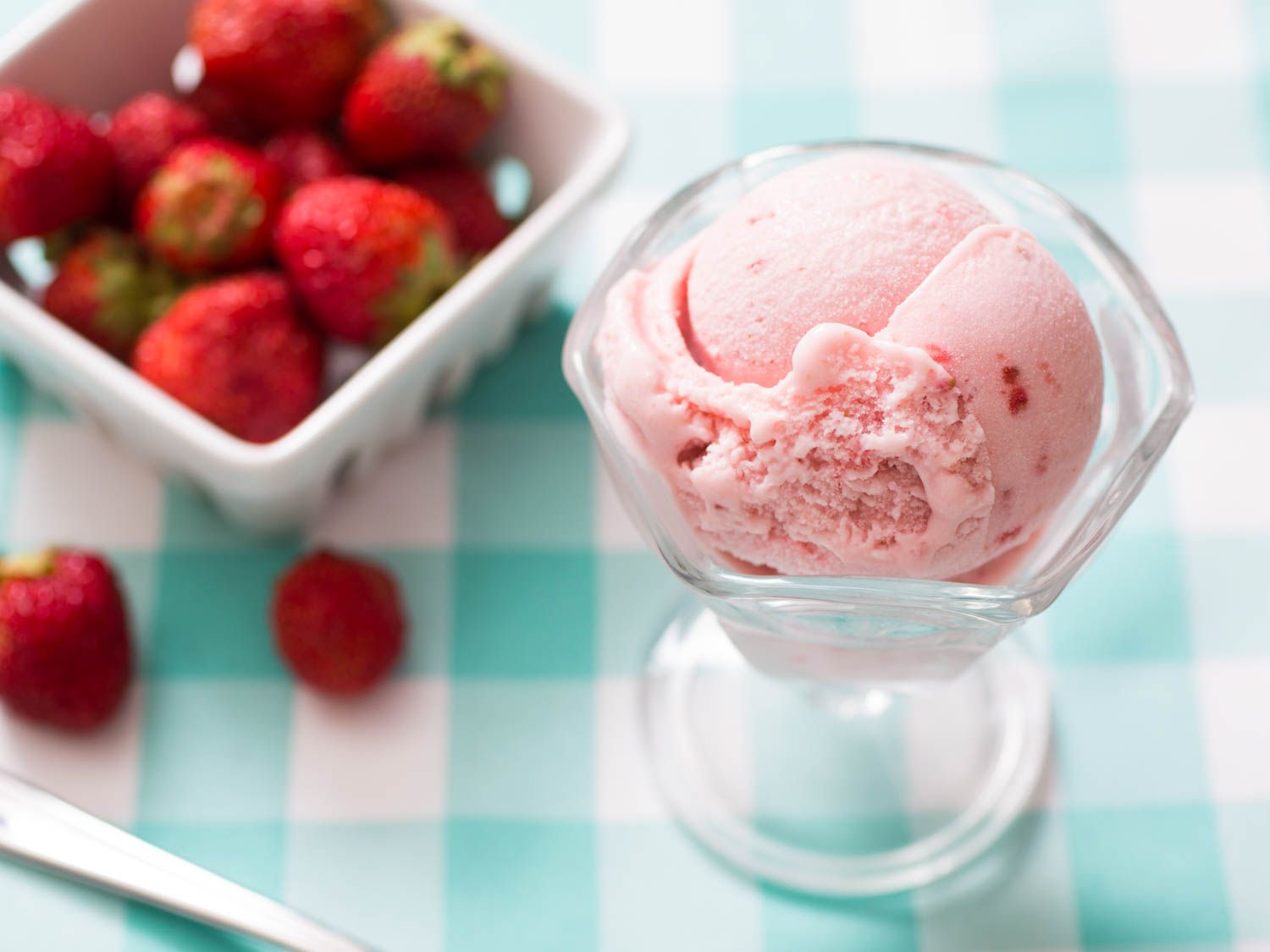 A scoop of strawberry ice cream in a footed glass dish next to a container of strawberries.