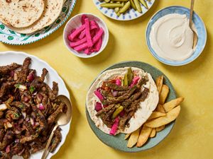 Beef shawarma wrap with accompaniments including pickles tahini sauce and pita bread on a table
