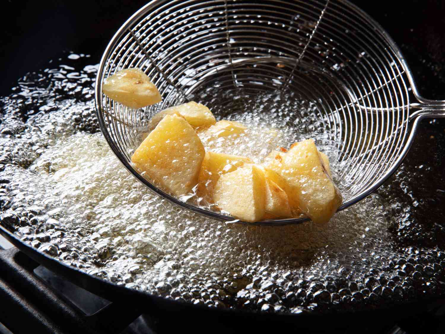 Yukon gold pieces being lifted out of hot oil with a spider skimmer