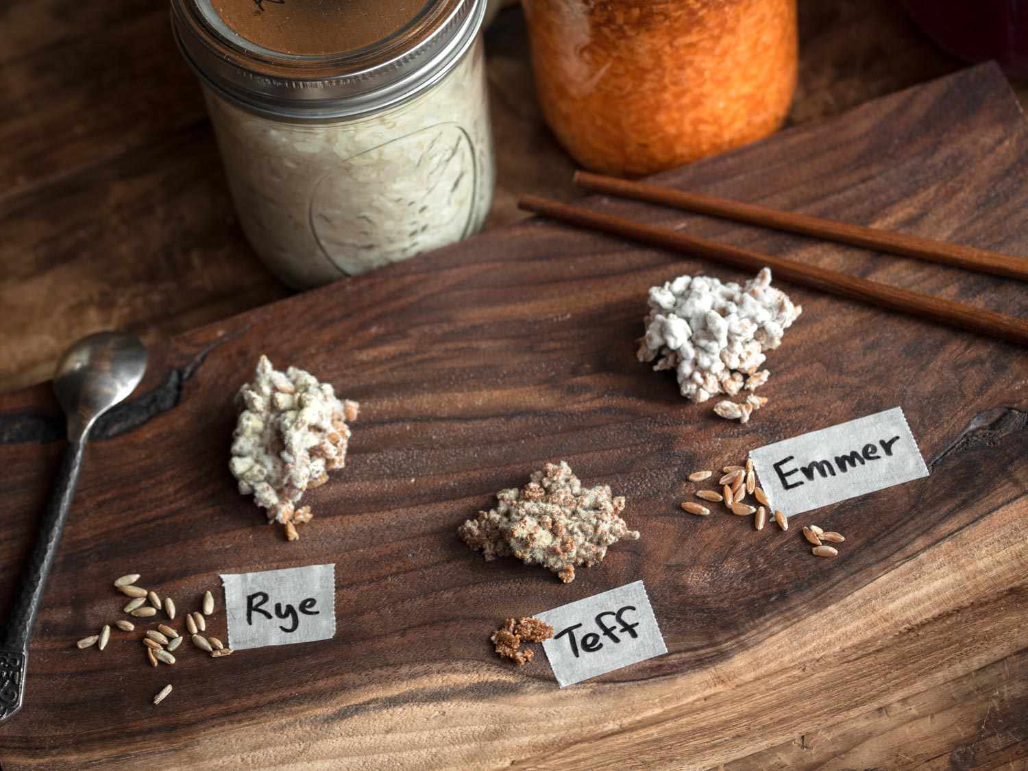 Koji made from rye, teff, and emmer, sitting on a wooden cutting board. There are labels beneath each koji sample indicating the name of each.