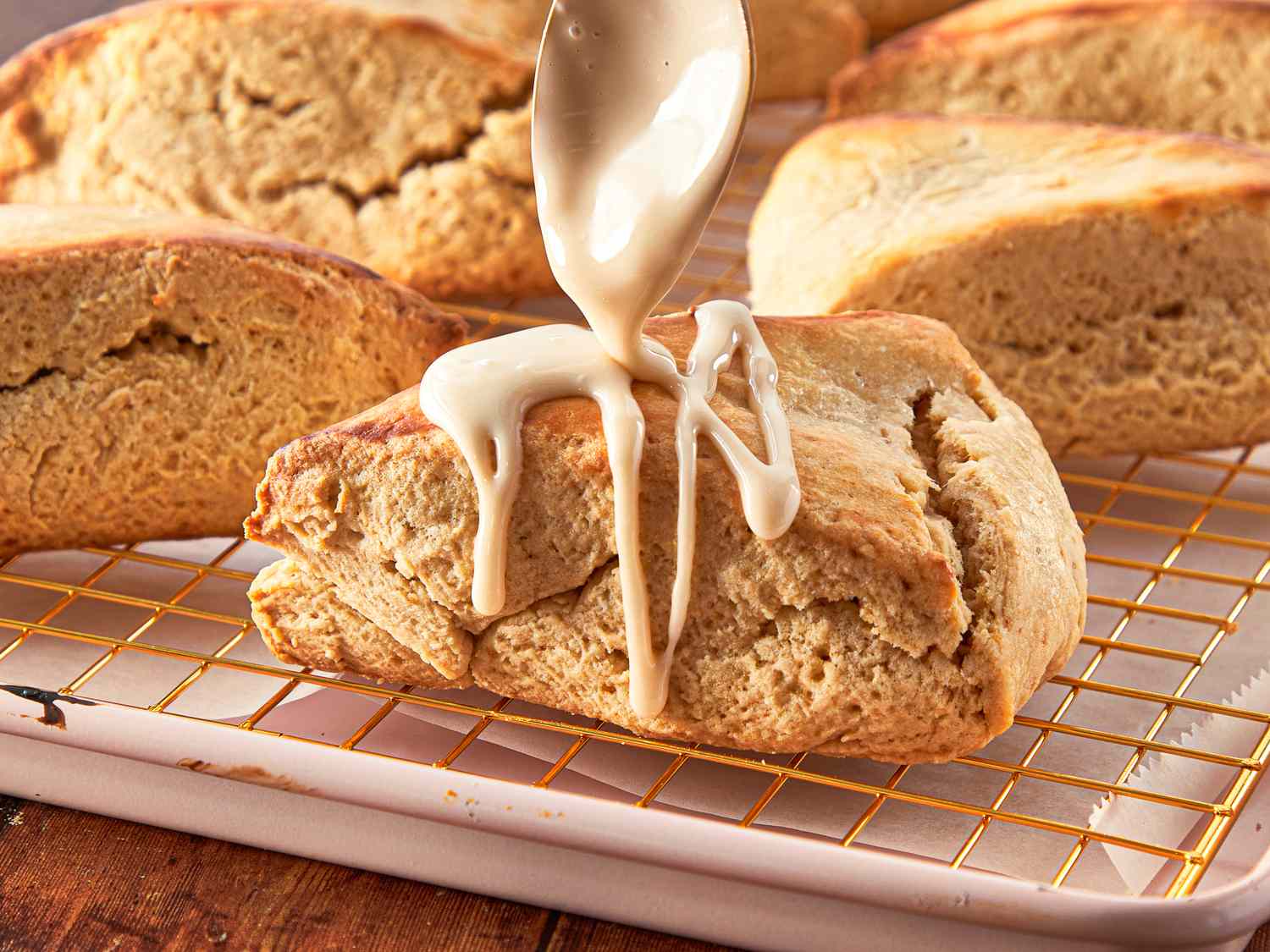 Maple scone being drizzled with glaze displayed on a cooling rack with other scones in the background