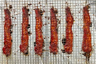 Six strips of seasoned bacon on a wire rack for cooking
