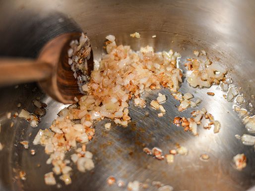Closeup of chopped shallot getting lightly browned in a saucepan.