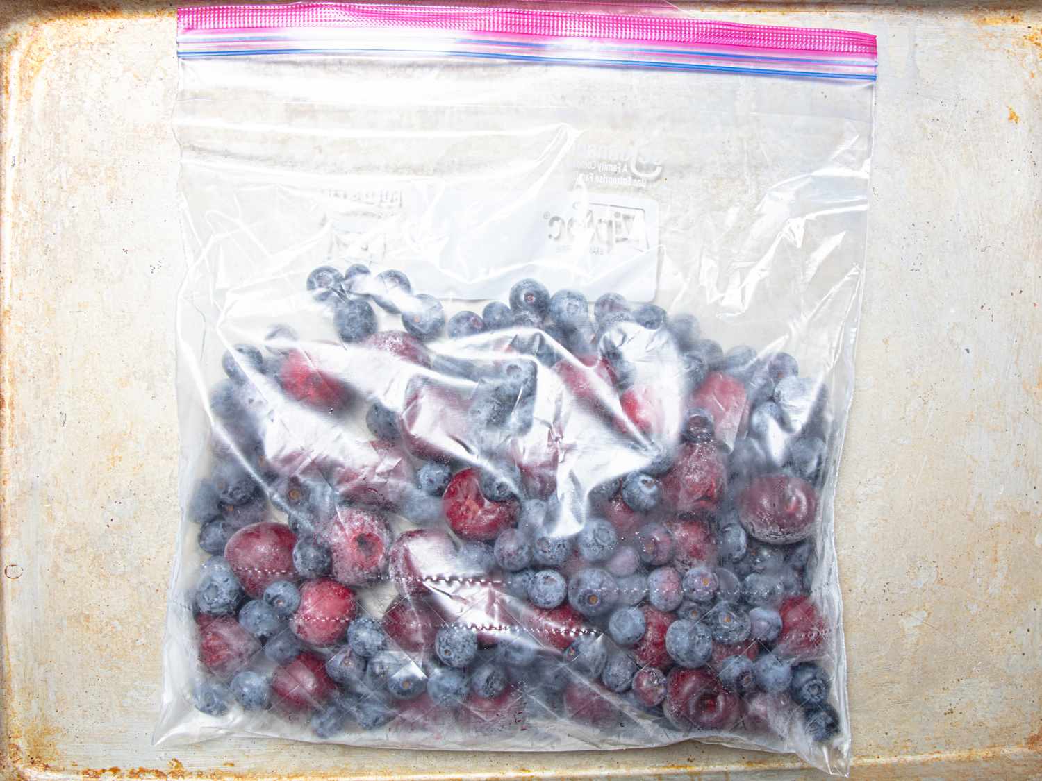 A resealable plastic bag containing frozen blueberries and raspberries on a light surface