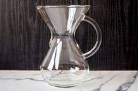 A clear glass Chemex coffee maker placed on a marble surface