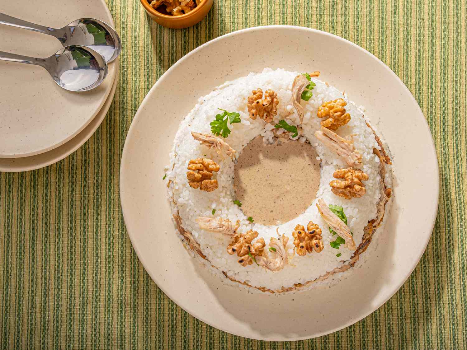 A plated dish presentation of Circassian chicken topped with walnuts and garnished arranged in a circular shape on a table