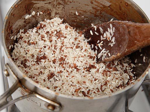 Toasting rice in coconut oil and browned coconut solids in a saucepan.