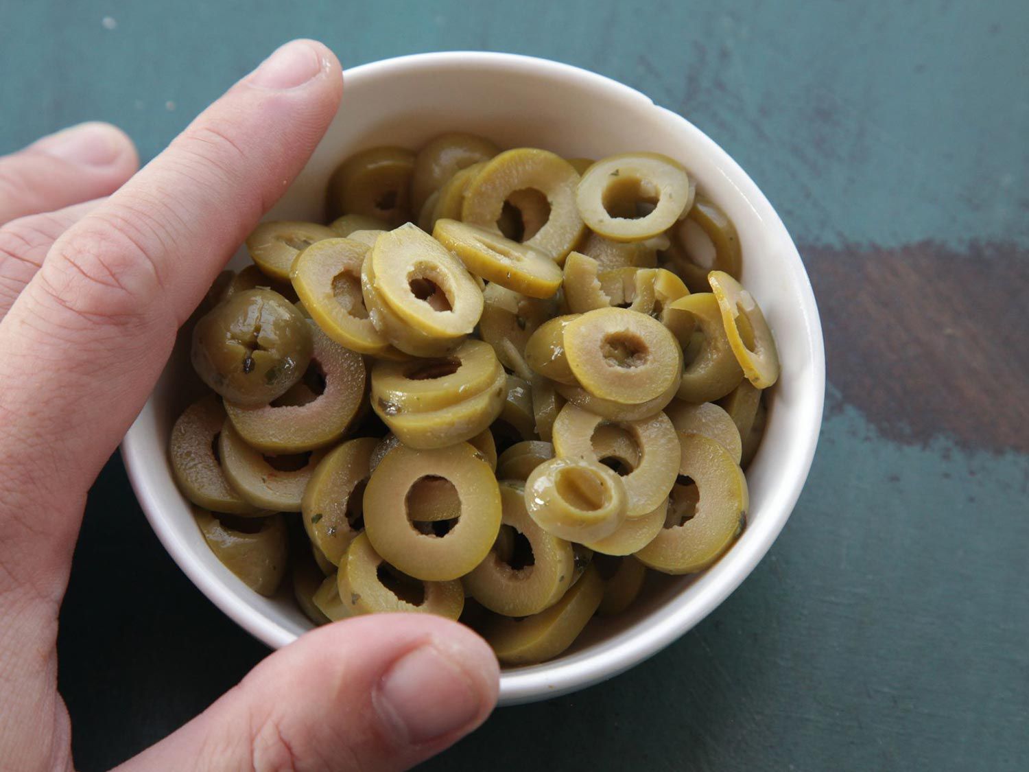 Hand holding bowl filled with sliced green olives