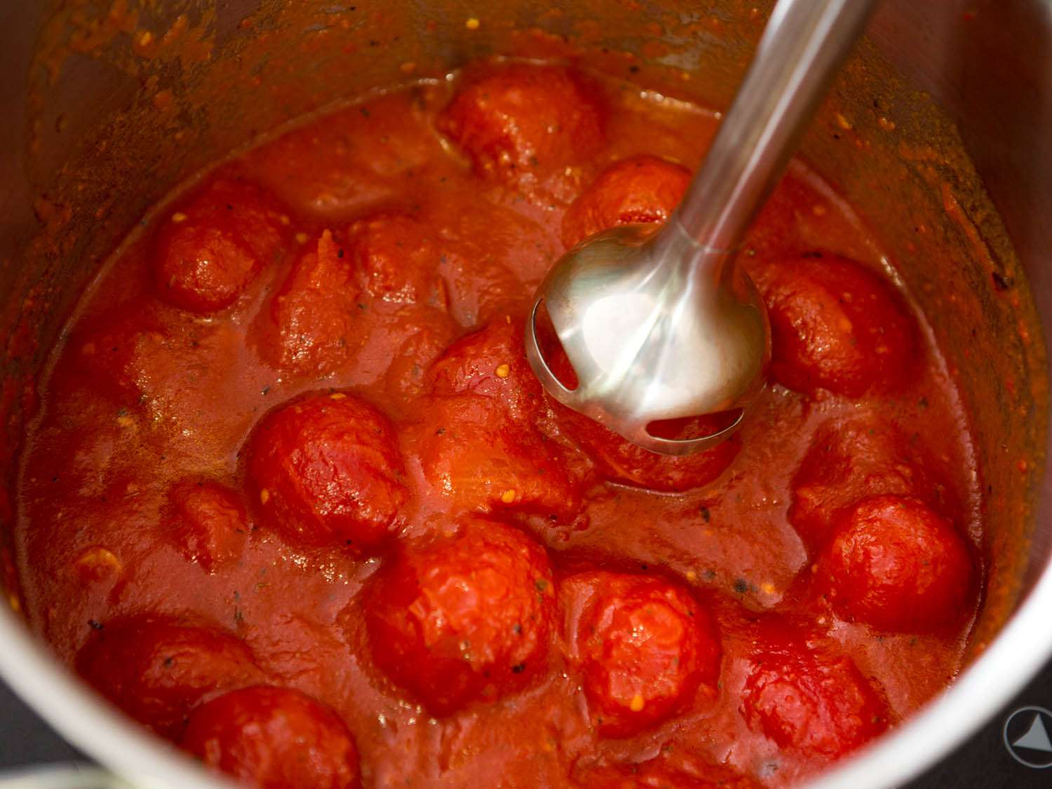 Using an immersion blender to puree canned tomatoes for quick Italian-American red sauce.