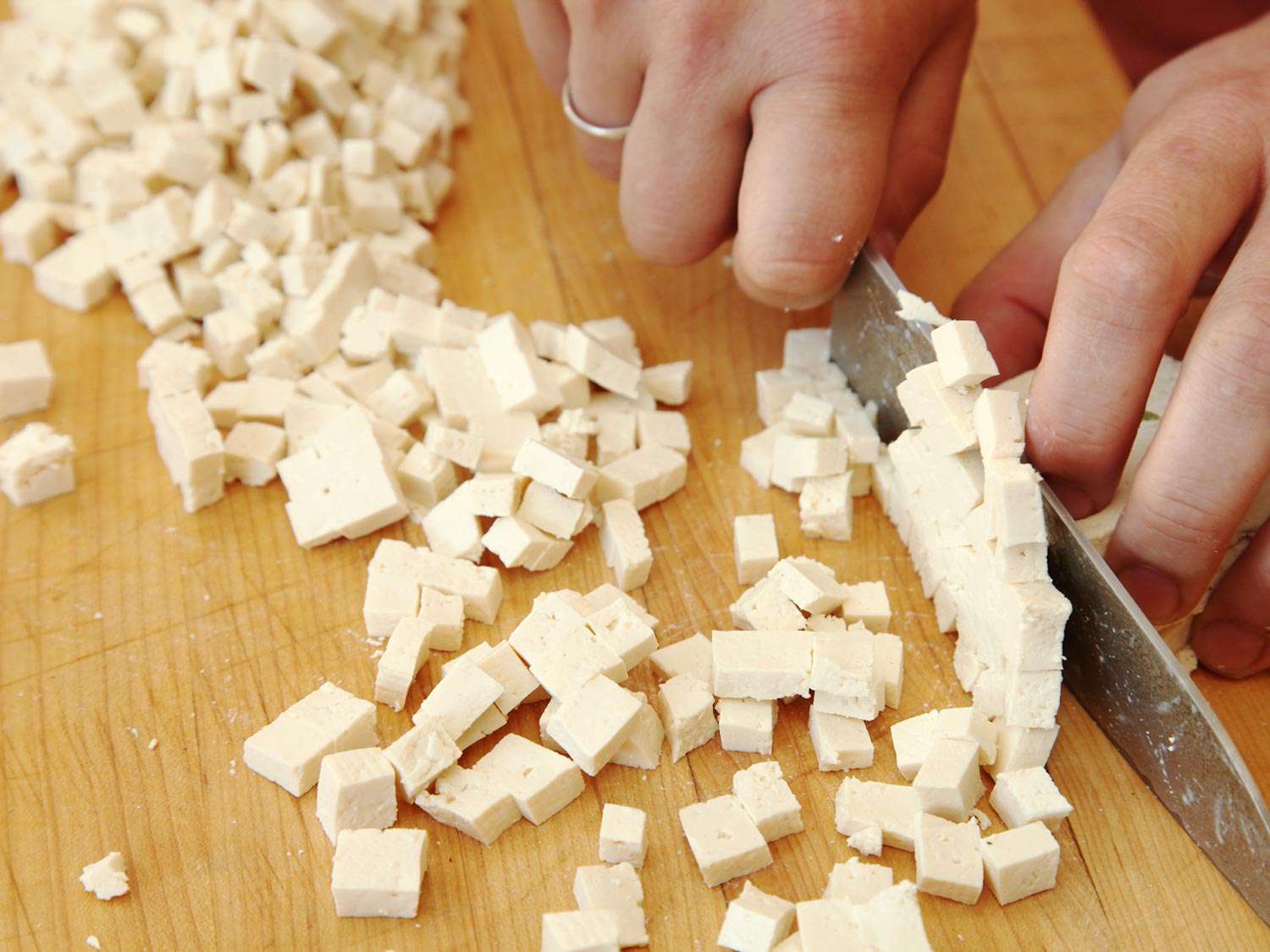 Tofu is cut into 1/4-inch dice on a cutting board.