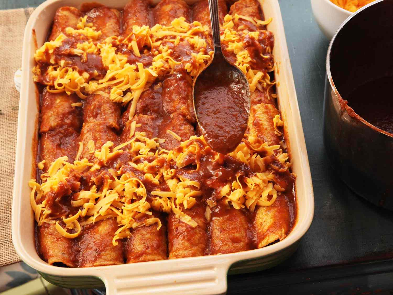 Adding sauce on top of cheese for enchilada in a baking dish. 