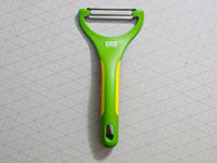A green kuhn rikon peeler on a grey surface