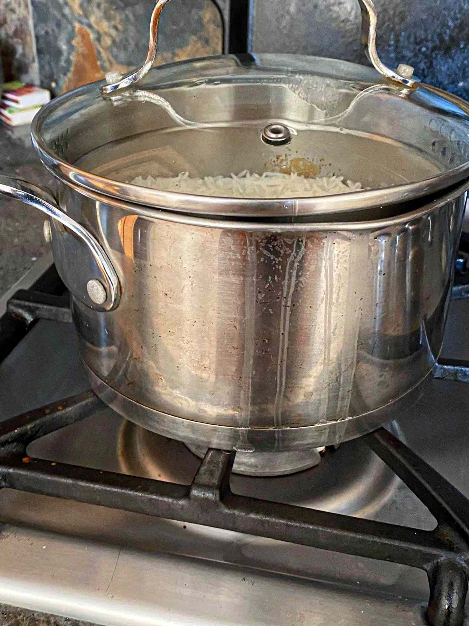 A metal pot with a lid is on a stovetop with rice visible inside