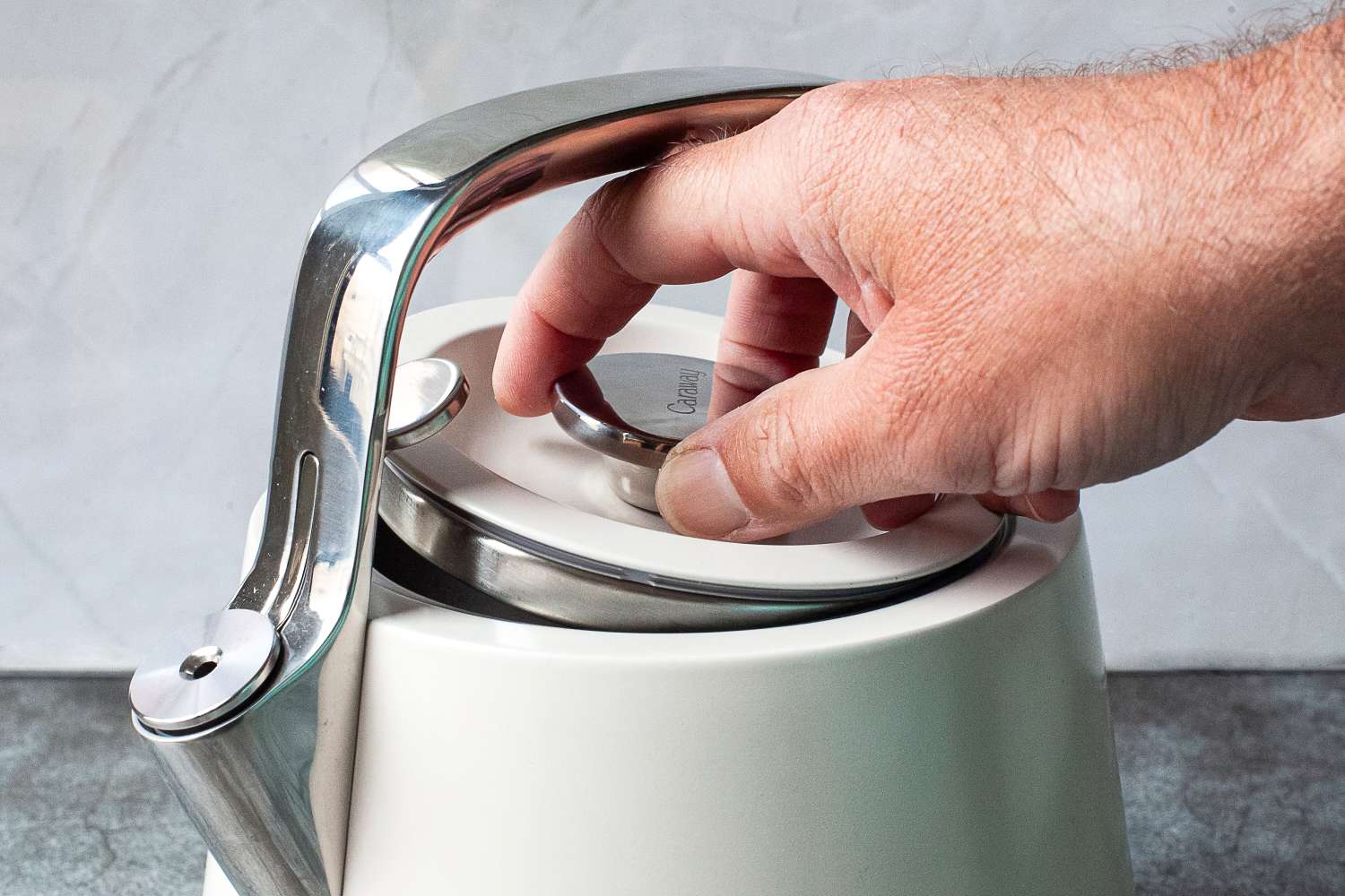 A hand lifting the lid of a kettle with a polished metal handle