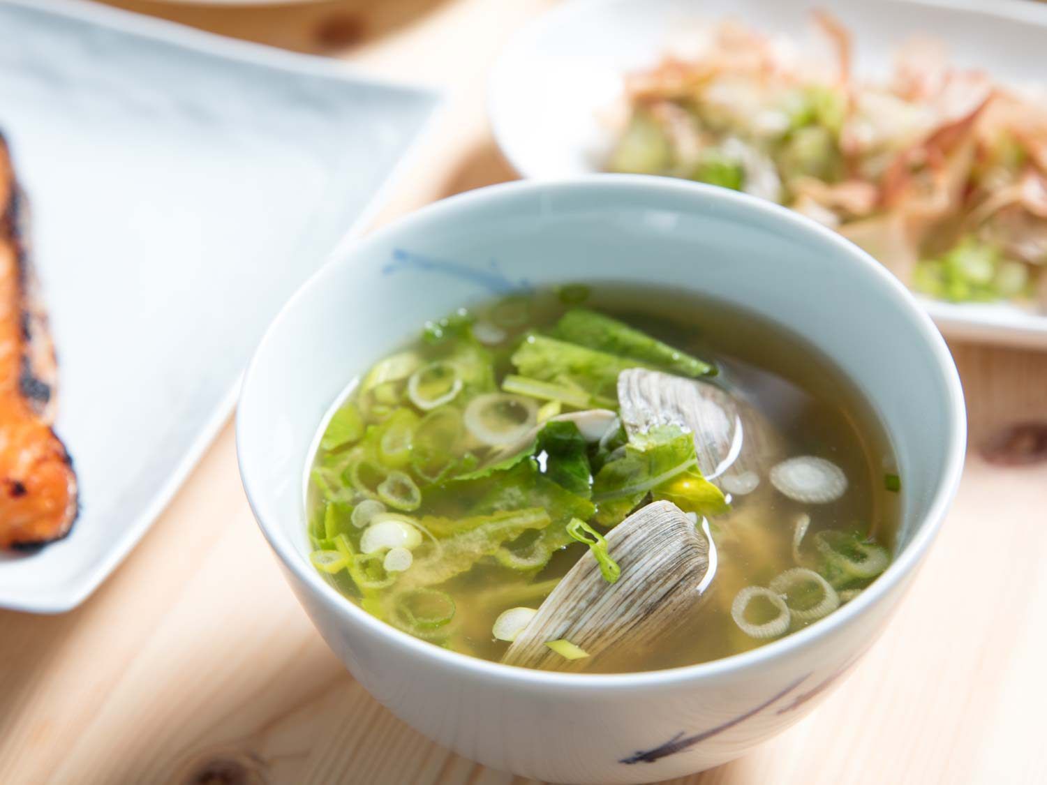 A bowl of miso soup with clams and scallions.