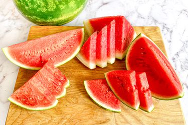 Sliced watermelon sitting on a wooden cutting board. 