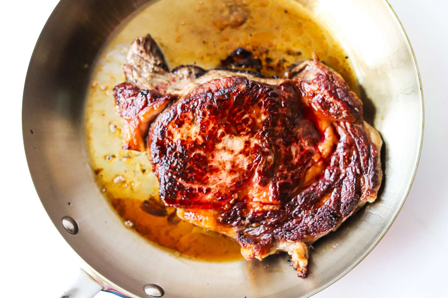 A panseared steak in a skillet with juices visible