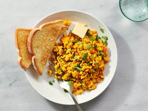 The anda bhurji on a white ceramic plate with toasted white bread and a pat of butter on a stone counter 