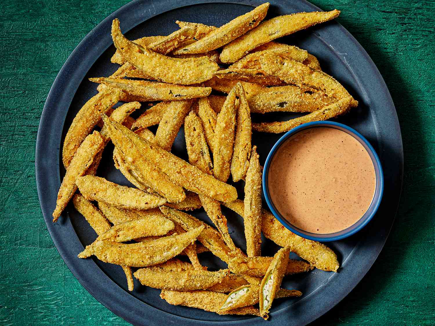 Dark blue plate with fried okra and a bowl of comeback sauce, on a deep green surface