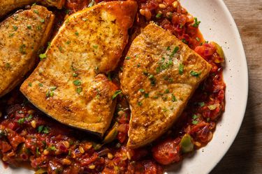 Deeply browned braised swordfish steaks on a platter with a rich tomato, caper, olive sauce.