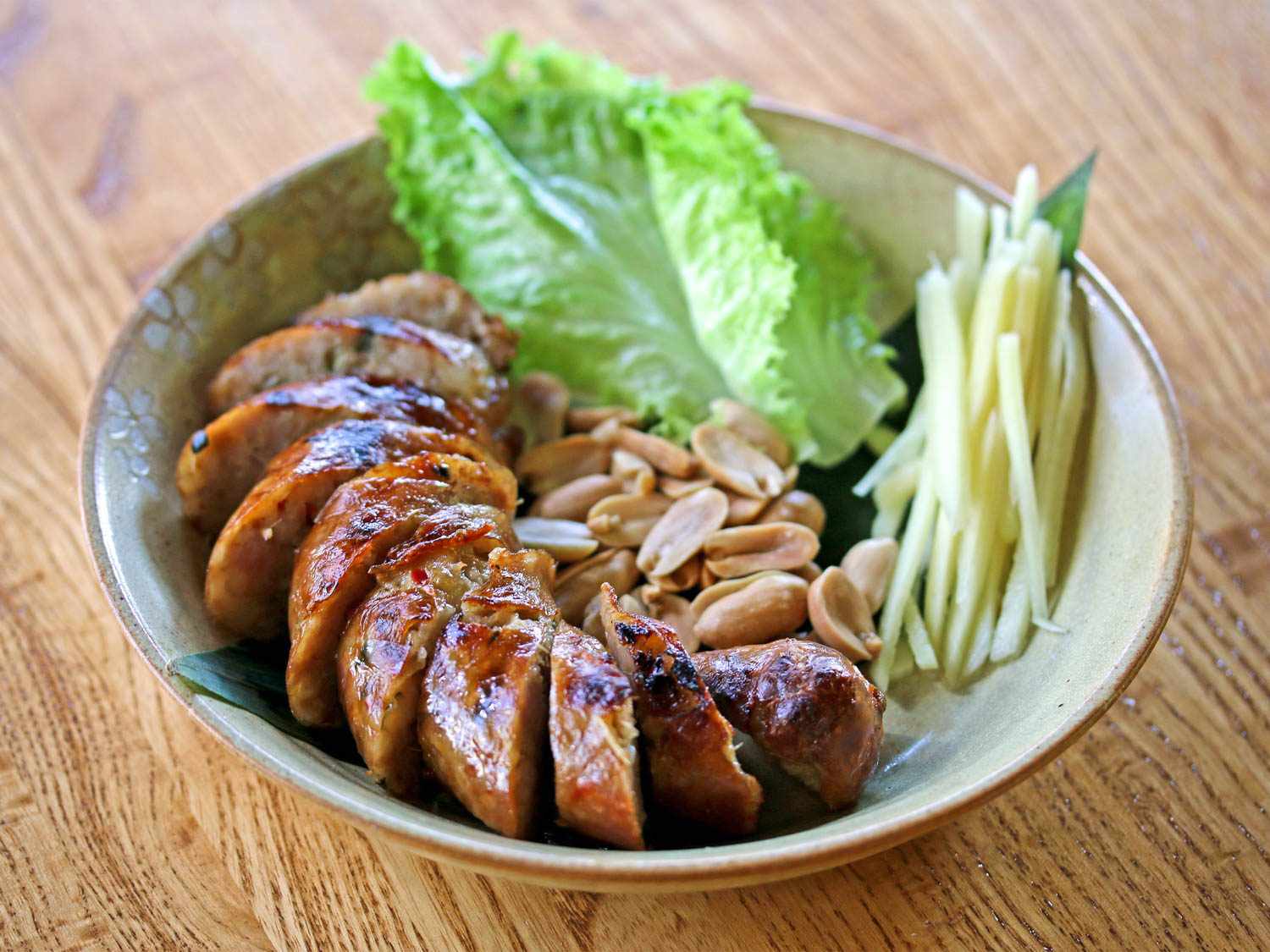 A stoneware bowl with slices of herbed pork sausage (sai oua) and raw vegetables.
