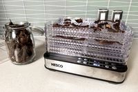 Nesco Digital 5 Rectangular Dehydrator with trays of dried food next to a jar of dried snacks