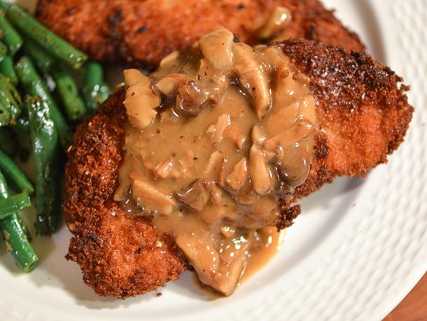 Breaded fried pork chop smothered in mushroom gravy on a plate.