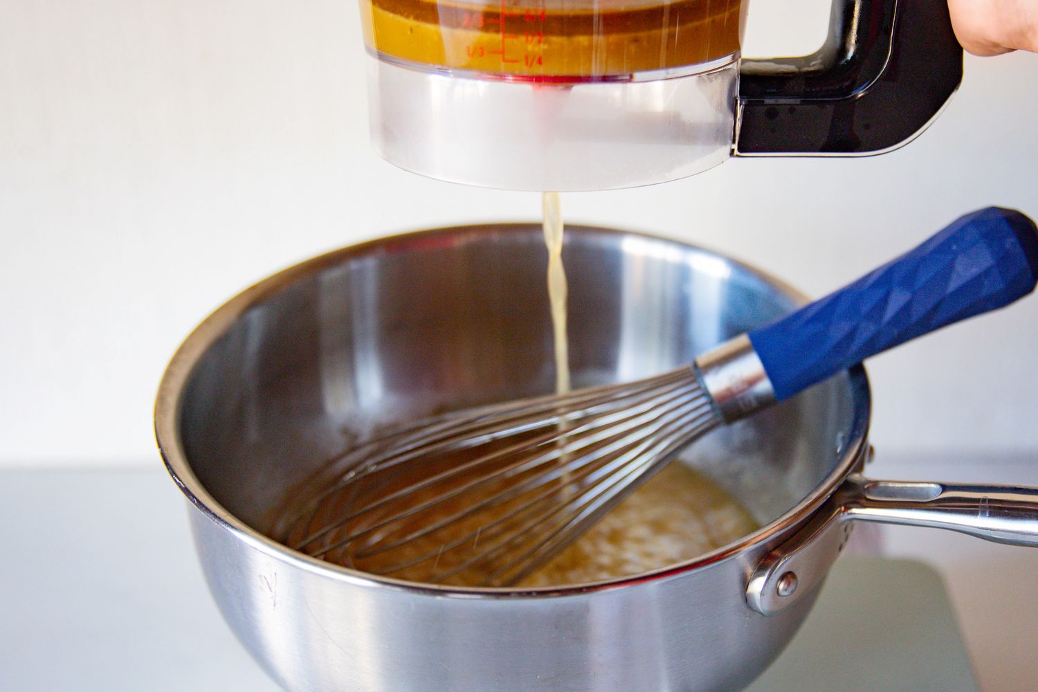 Liquid being poured into a mixing bowl containing a whisk