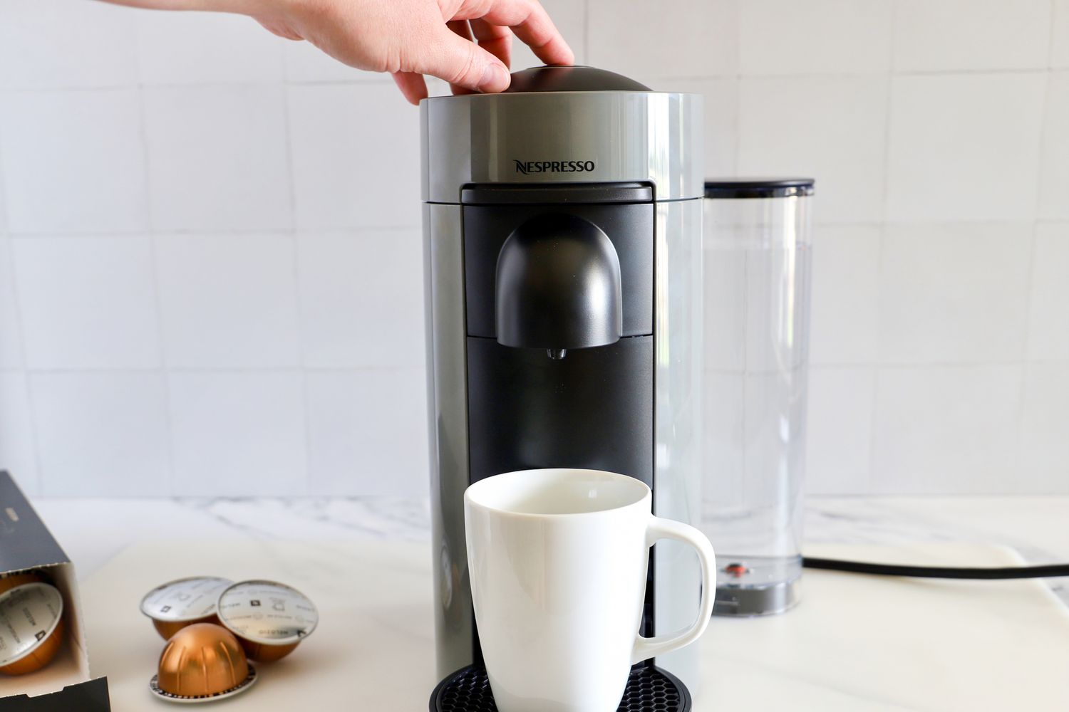 A hand pressing the top of the Nespresso VertuoPlus Coffee and Espresso Machine by De'Longhi