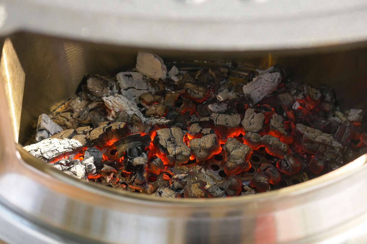 Burning embers and charcoal in a metal fire pit glowing orange