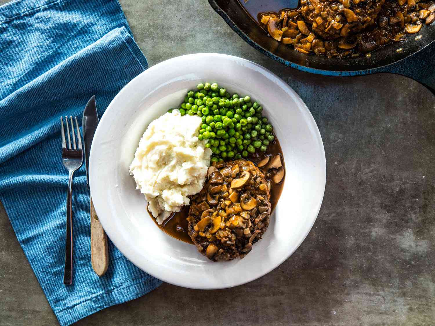 Overhead view of a finished serving of Salisbury steak, plated with mashed potatoes and green peas.