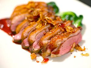 Sliced seared sous vide duck breast on a white plate with sauce and sautéed greens.