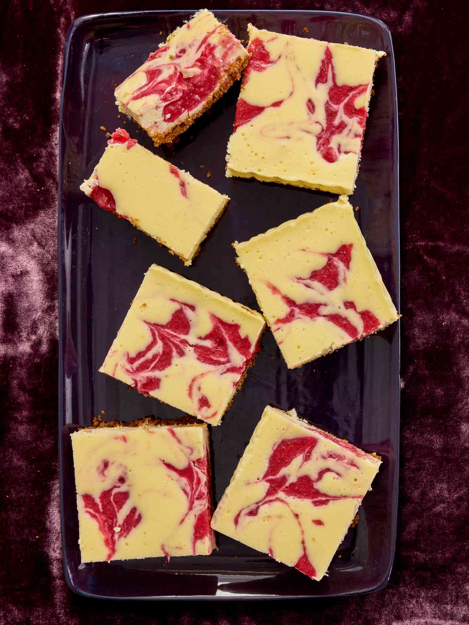 Strawberry cheesecake bars in a purple tray, on purple velvet 