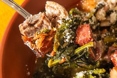 A spoonful of Italian wedding soup featuring meat greens and small pasta in a broth