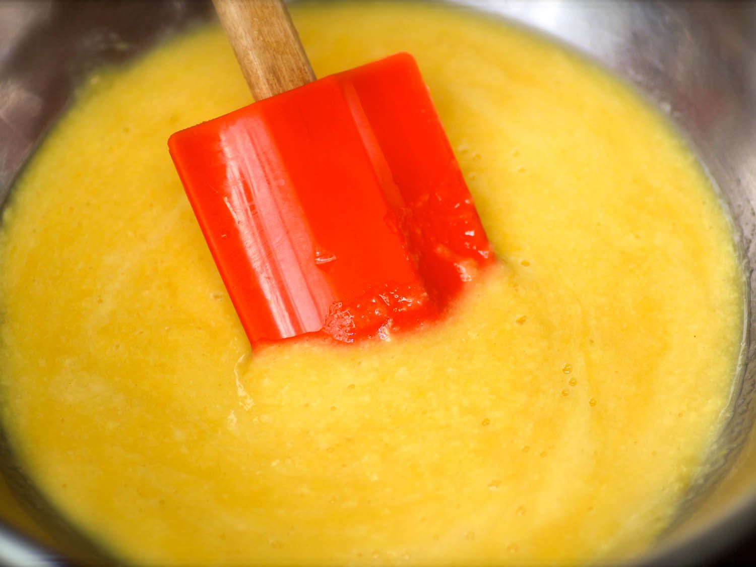Pawpaws pulp in a metal bowl being stirred with a spatula 