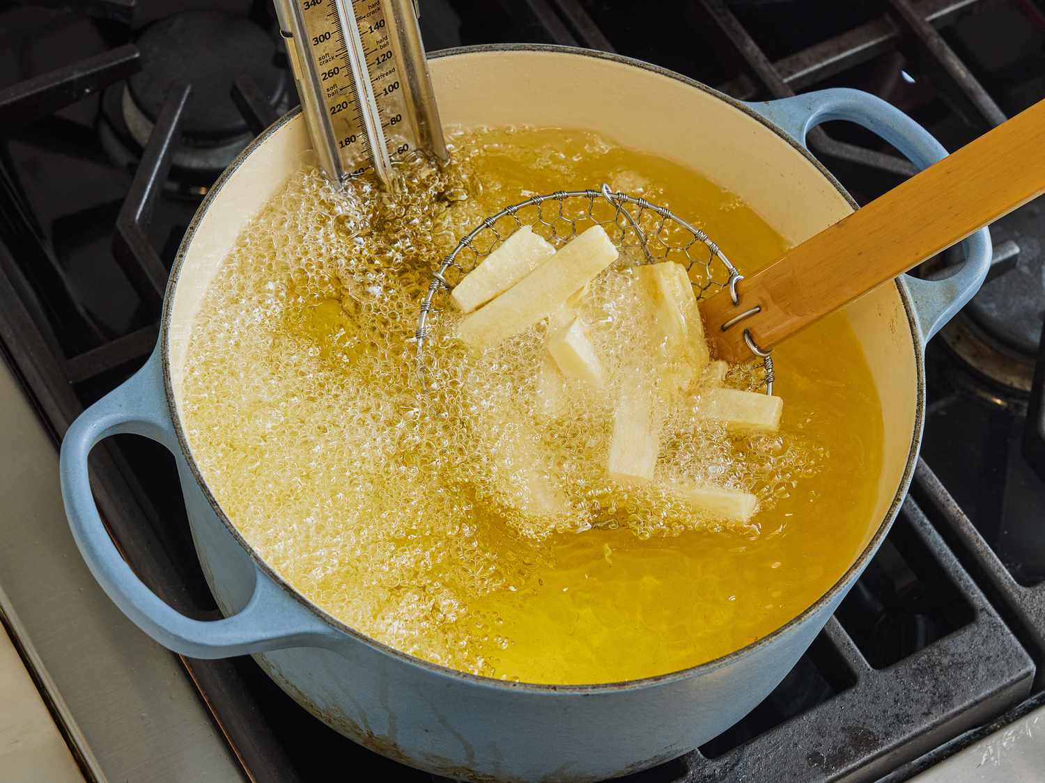 Dipping sliced yuca into dutch oven of hot oil