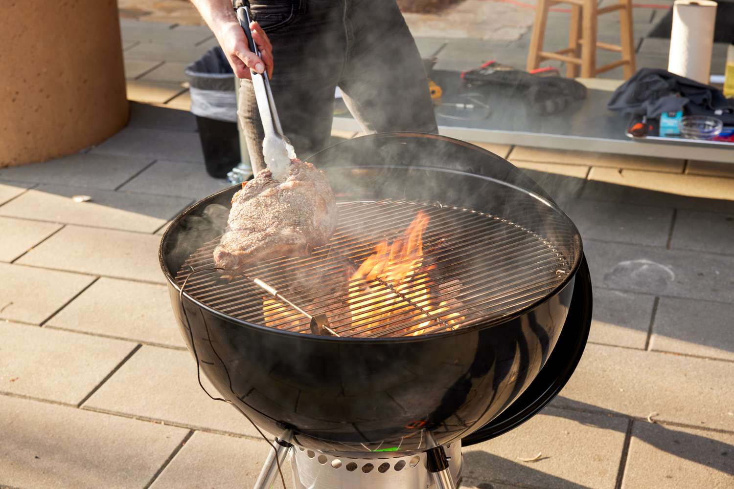 A person grilling a steak on a Weber charcoal grill.