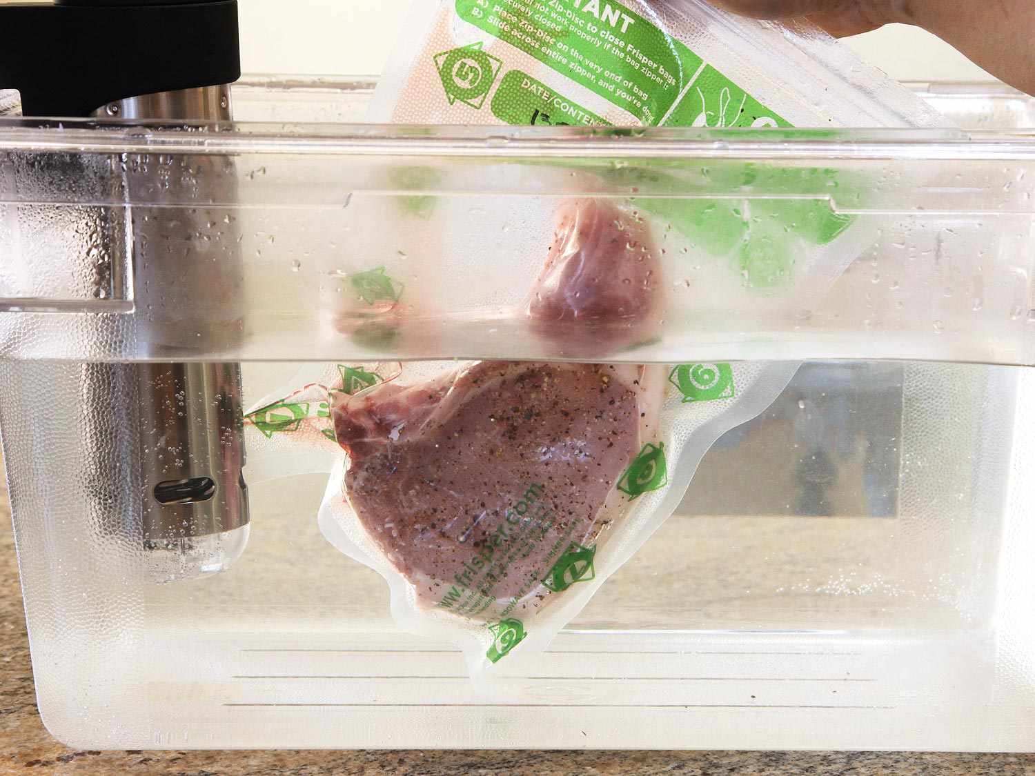 Vacuum-sealed pork chop being placed in a water bath to be cooked sous vide.