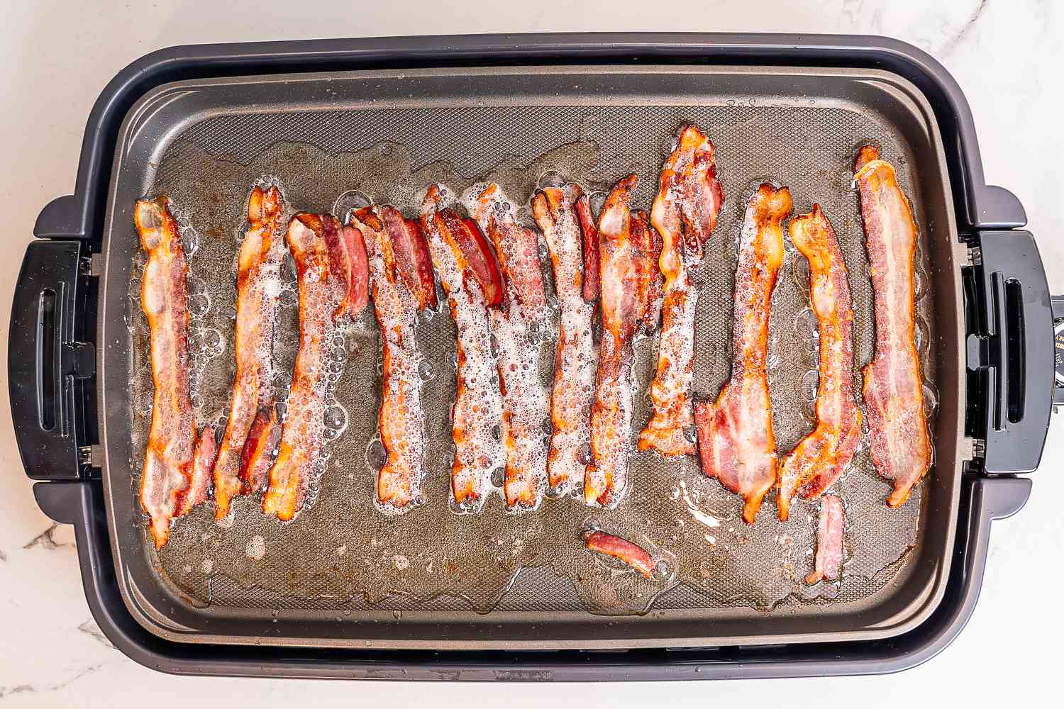 An electric griddle filled with bacon cooking