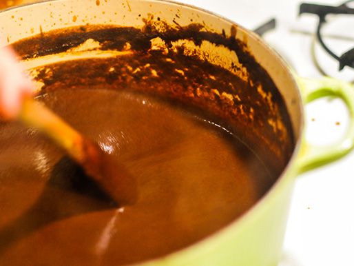 Chile purée and a spice mixture being cooked in a Dutch oven and stirred with a wooden spoon. 