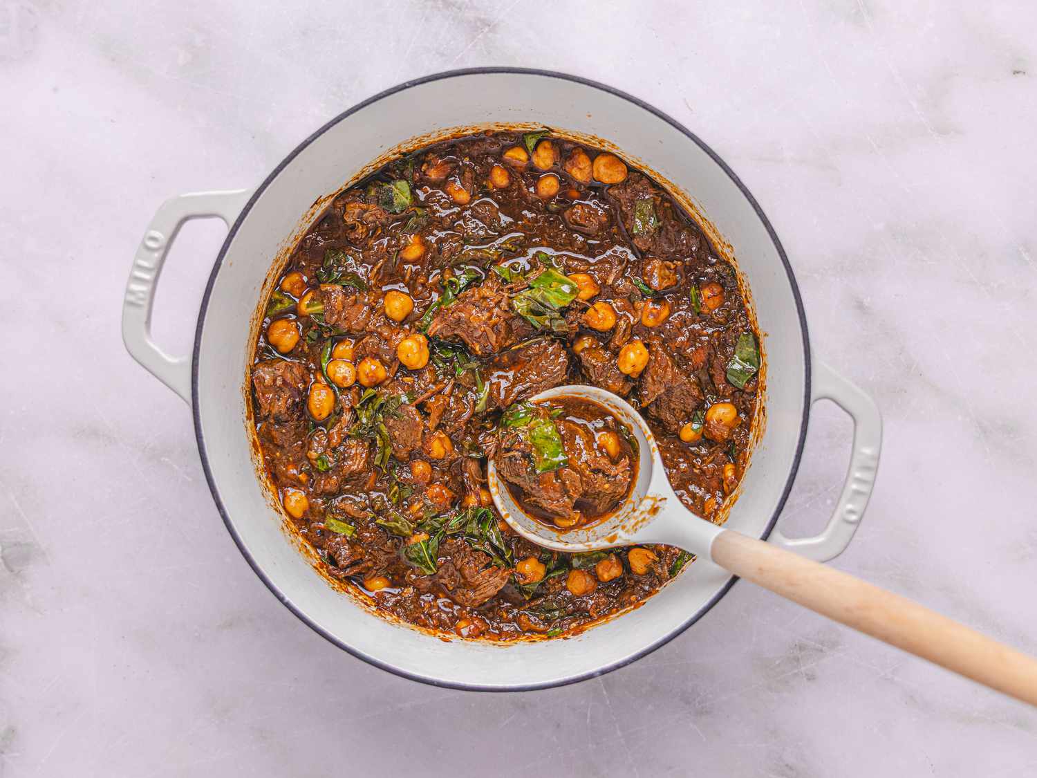 spoon in cooked stew in a dutch oven on a white marble surface 