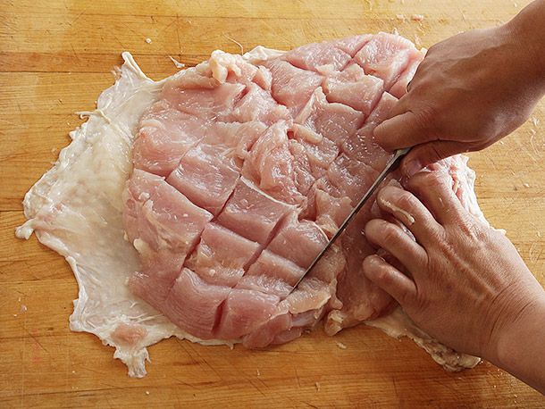 Using a boning knife to cut diagonal slashes in turkey breast.