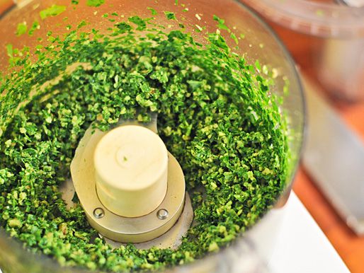 Closeup of food processor bowl filled with puréed arugula.