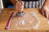 A hand using a short-handled meat pounder to flatten a chicken breast
