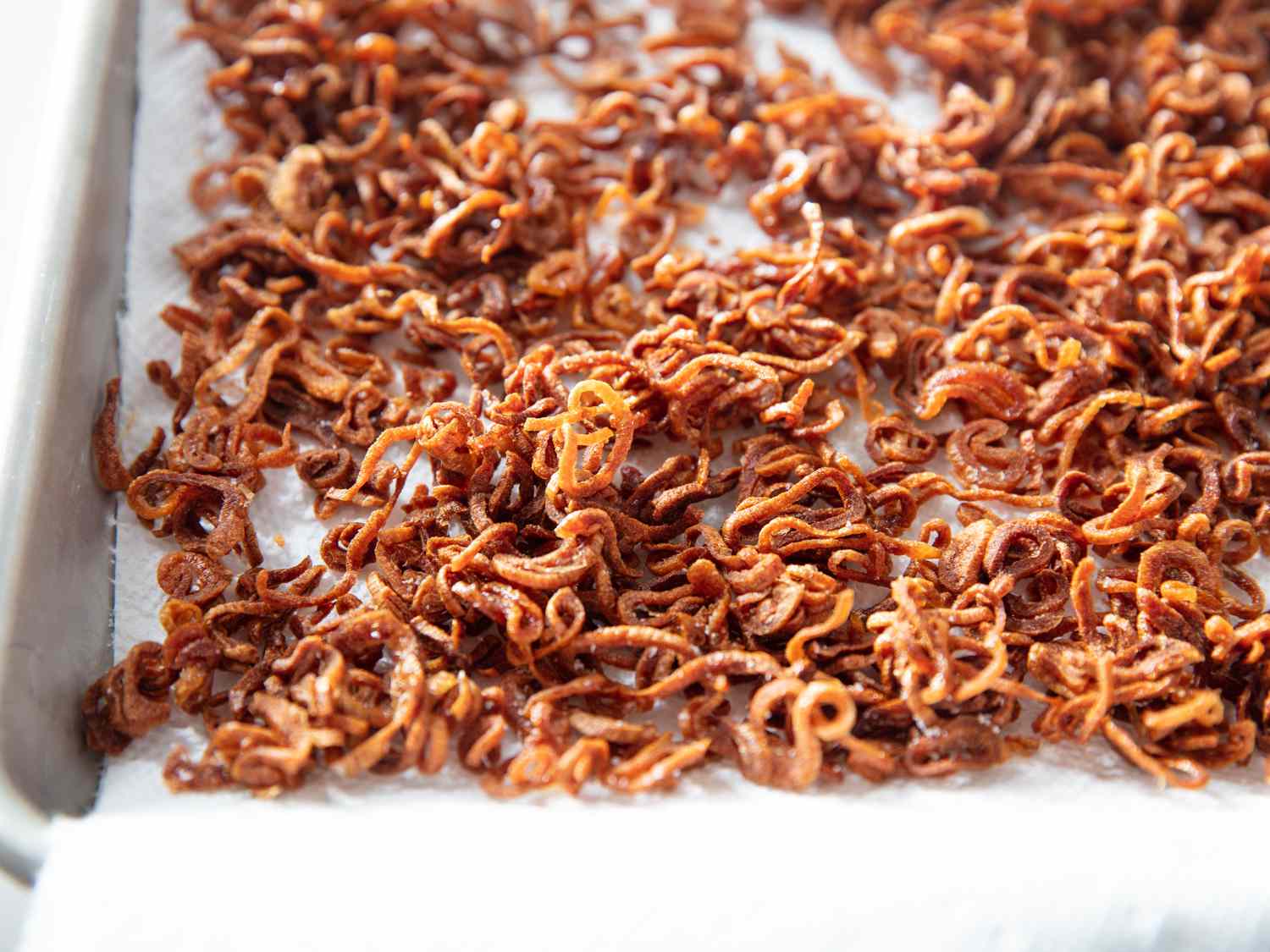 The finished shallots, browned and crispy, are drained on a paper towel-lined sheet pan.