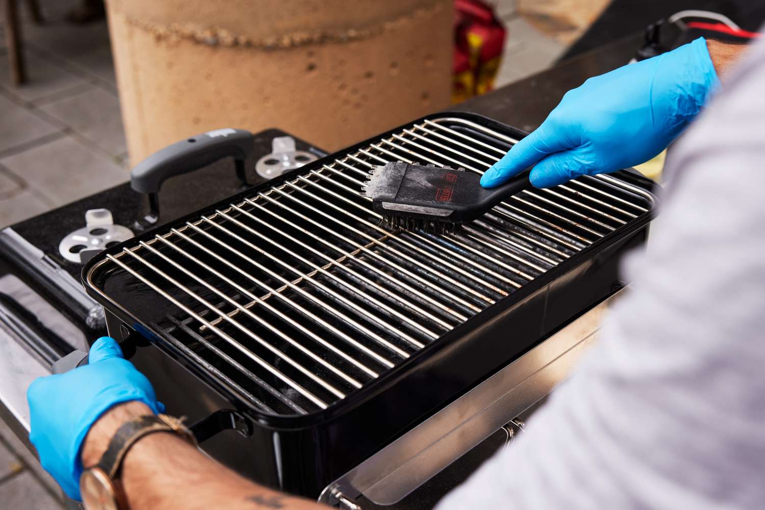 A person cleaning the Weber's grill grates with a grill brush.