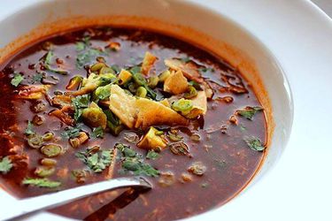 Closeup of a bowl of turkey tortilla soup, garnished with crumbled tortilla chips, cilantro, and avocado.