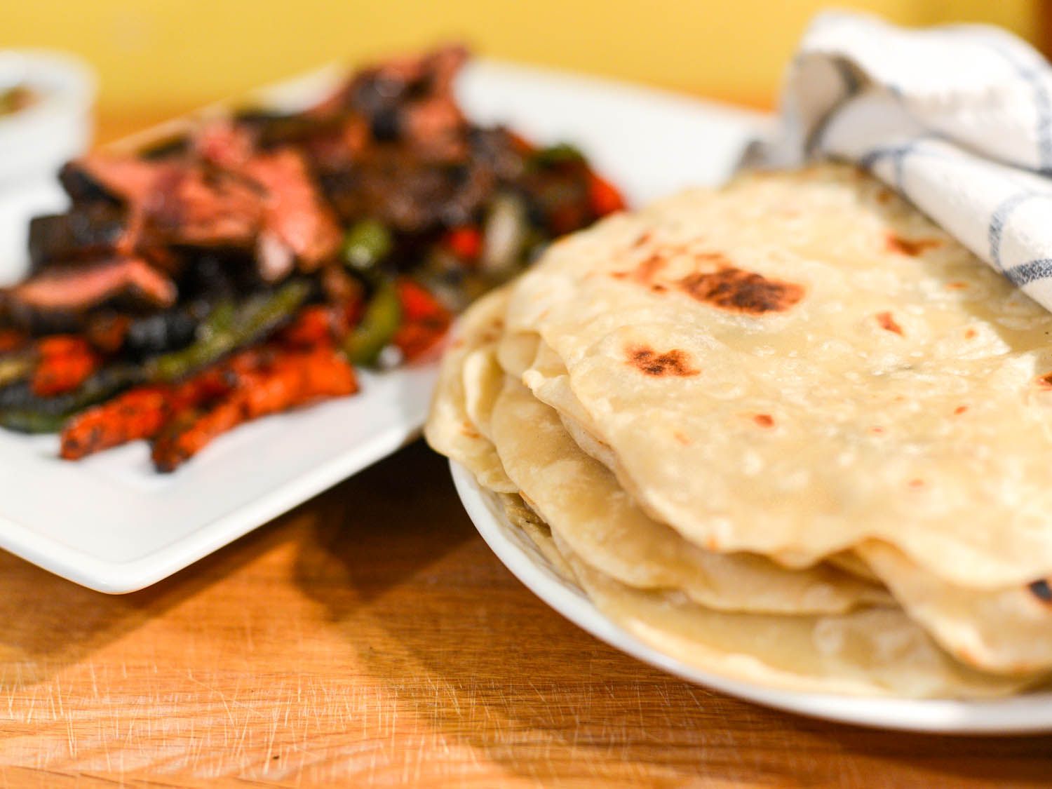 A stack of thin flour tortilla next to a platter of steak fajita.