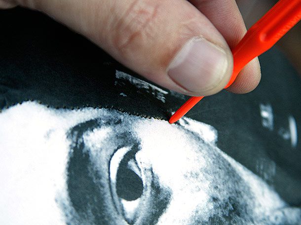 Using a small red punch tool to poke holes in a photo laid over a pumpkin for carving